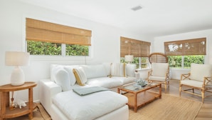 Uma sala de estar moderna com um sofá branco, duas poltronas, uma mesa de centro e uma mesinha de apoio com uma luminária.
