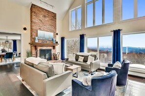 A spacious living room with a brick fireplace, large windows, and a view of the outdoors.