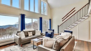 A spacious living room with a large window, a staircase, and a view of the outdoors. - Stoweic Views  - Luxury Dream Vacation Home (Stowe)