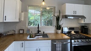 Et moderne køkken med hvide skabe, en ovn i rustfrit stål og et vindue med udsigt til grønne områder.