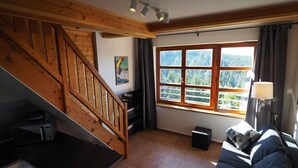 A room with a wooden staircase, a large window with a view of trees, a sofa, and a lamp. - Cihlarka Mountain View Apartment (Cerny Dul)