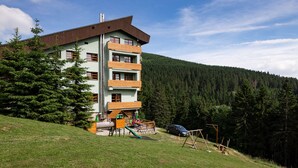 A multi-story building with a sloped roof, a children's play area with slides and swings, and a car parked in front. - Cihlarka Mountain View Apartment (Cerny Dul)