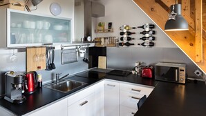 A modern kitchen with a large window, a coffee maker, a toaster, and wine bottles on the wall. - Cihlarka Mountain View Apartment (Cerny Dul)