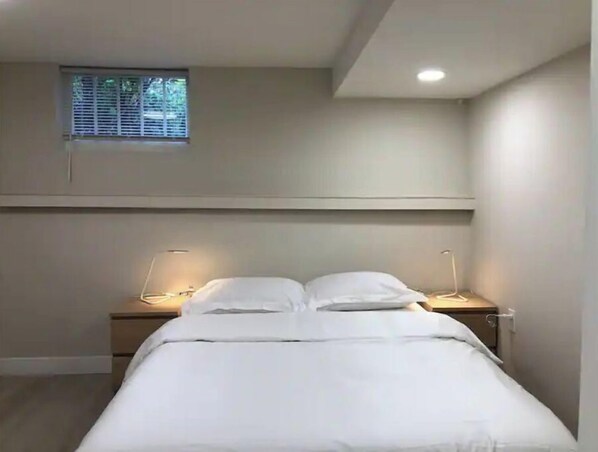 A bedroom with a bed, bedside tables, and a window.