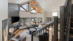 A spacious living area with a fireplace, large windows, a staircase, and a modern design. - Valley Vista Retreat - New 5BR Cabin (Lead)