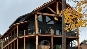 A modern two-story cabin with a stone foundation, wooden beams, and large windows. - Valley Vista Retreat - New 5BR Cabin (Lead)
