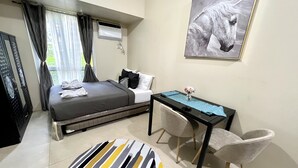 A hotel room with a bed, a desk, a chair, a painting, and a bathroom with a shower.