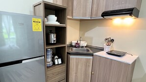 A compact kitchen with a built-in refrigerator, wooden cabinets, a microwave, a kettle, and a sink.