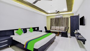 A modern hotel room with a large bed, bedside tables, a desk, a chair, a TV, and a ceiling fan. - Treebo Baby Pearl (Amravati)