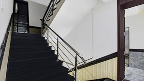 A staircase with black steps and a metal railing, leading to a landing with a wooden panel wall. - Treebo Baby Pearl (Amravati)