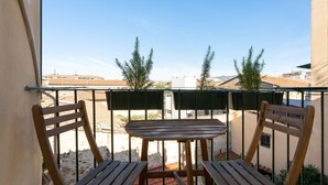 A balcony with a wooden table and two chairs, overlooking a sandy area with buildings in the background. - Porcellana Apartment (Firenze)