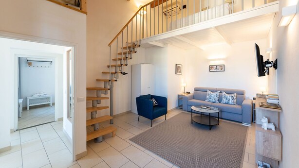 A modern living room with a staircase, a sofa, a coffee table, and a TV. - Porcellana Apartment (Firenze)