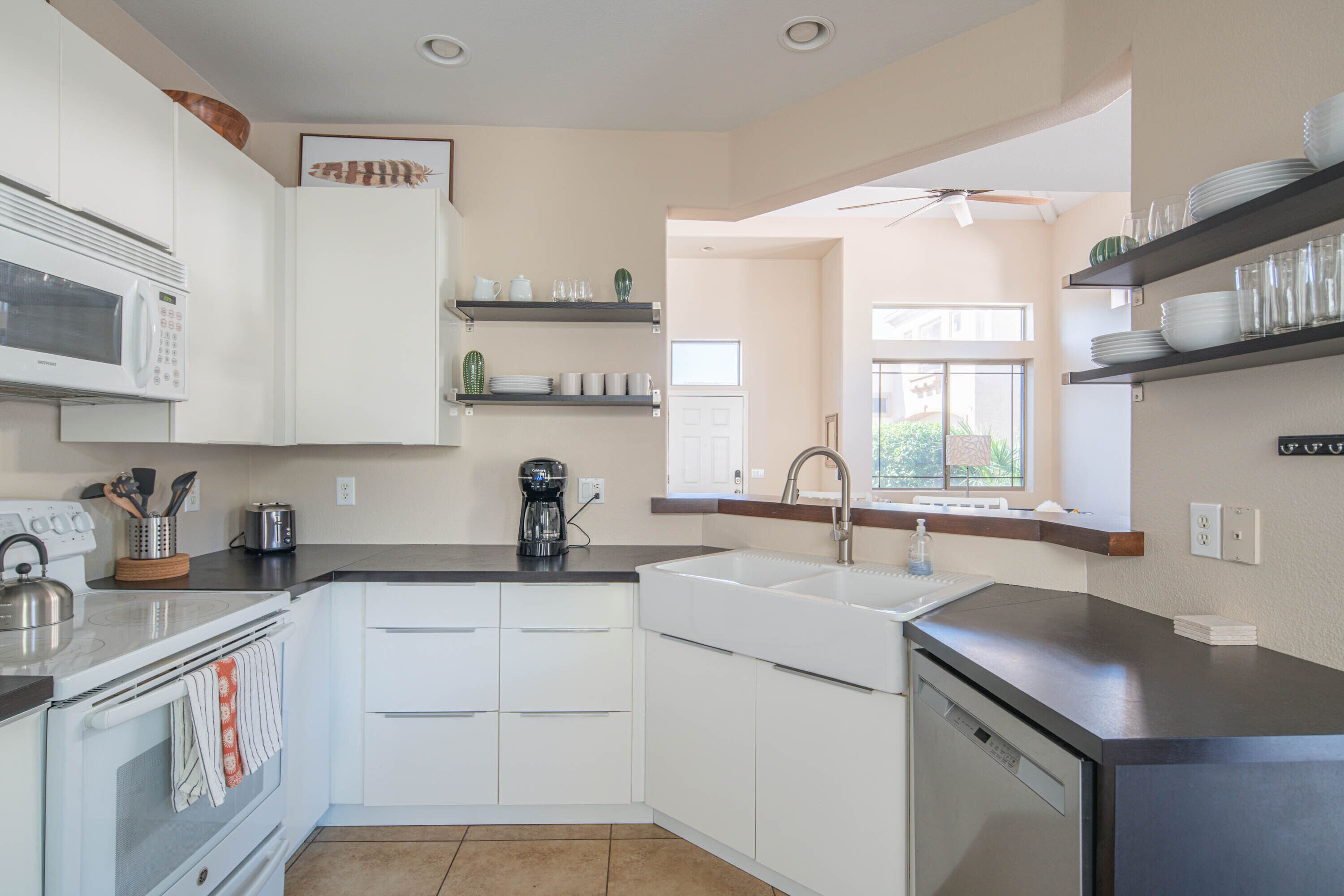 A modern kitchen with white cabinets, a black countertop, a microwave, a coffee maker, and a dishwasher.