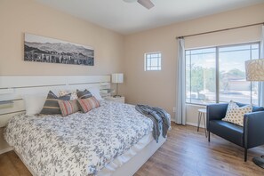 A bedroom with a large bed, a nightstand, a bedside table, a window with curtains, and a view of the outdoors. - Beautiful Cave Creek 3 Bdrm home in Quiet Area! (Cave Creek)