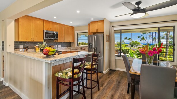 A modern kitchen with wooden cabinets, a large island, and a view of palm trees. - Tropical Oasis - Stunning Views In Private Setting (Princeville)