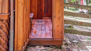 Eine hölzerne Sauna im Freien mit geneigtem Dach und einer Metalttür.