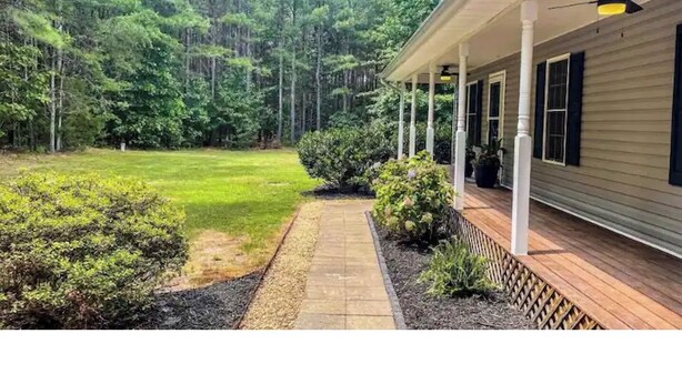 A house with a covered porch, a well-maintained lawn, and a dense forest in the background.