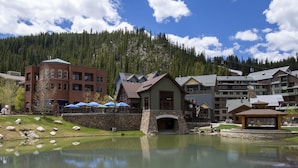 A lakeside hotel with a stone bridge, a gazebo, and a mountain backdrop.