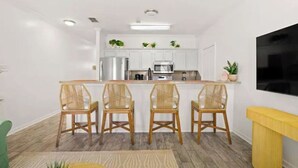 Une cuisine moderne avec des meubles blancs, un îlot central doté de chaises et un téléviseur à écran plat fixé au mur.