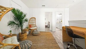 Une pièce moderne et bien éclairée, avec un fauteuil en osier, un bureau en bois et une grande plante en pot.