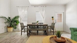 Un salon avec un plancher en bois, une table à manger avec des chaises, un canapé vert et une porte avec une fenêtre.