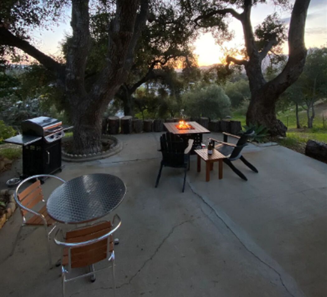 Un patio exterior con una parrilla, una mesa redonda y sillas.