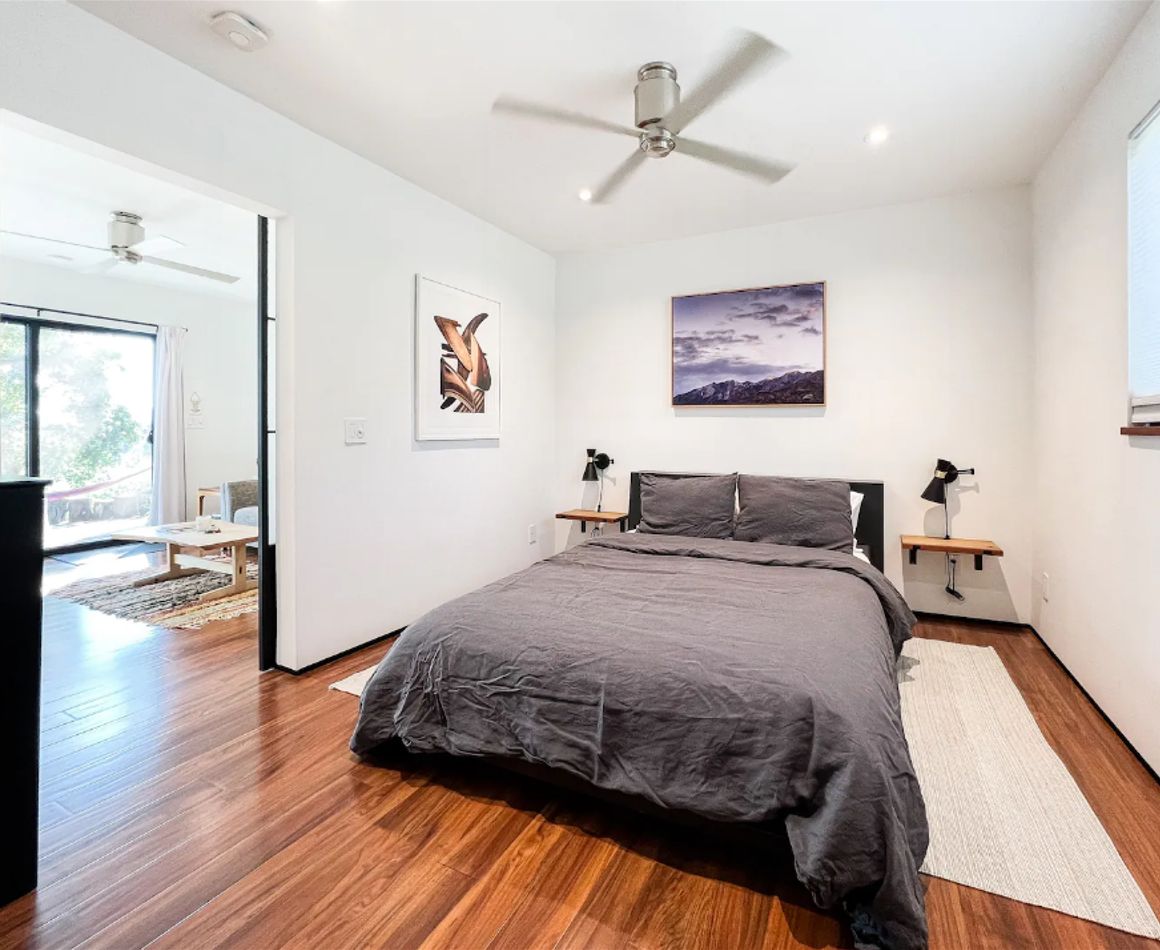 A modern bedroom with a large bed, a ceiling fan, and artwork on the walls.