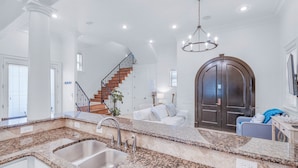 A spacious kitchen with granite countertops, a double sink, and a wooden staircase leading to a living area. - 🐟Three Master Suites- Pet Friendly-Seas the Day on 30A (Santa Rosa Beach)