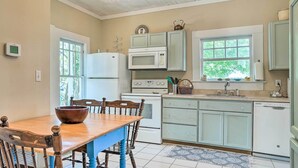 Una cocina con electrodomésticos blancos, una mesa de comedor de madera y una ventana con vistas a la vegetación.