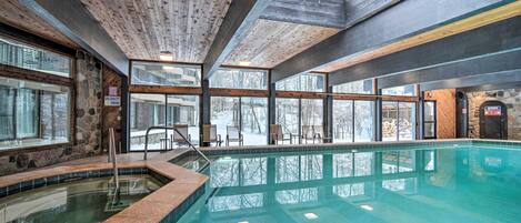 A large indoor swimming pool with clear glass walls, wooden ceiling beams, and stone accents.