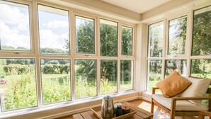 A sunlit room with large windows, a wooden table, and a cushioned chair.