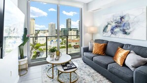 A modern living room with a grey sofa, a round coffee table, and a large window offering a city view. - Pool, Views 1BR Downtown Condo near Bayfront Park (Miami)