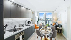 A modern kitchen with a large island, a dining area with a round table, and a view of the city through large windows. - Pool, Views 1BR Downtown Condo near Bayfront Park (Miami)