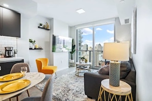 A modern living room with a dining area, a sofa, a coffee table, and a view of the city through large windows.