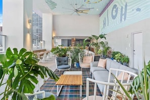 A modern lounge area with seating, plants, and a ceiling fan.