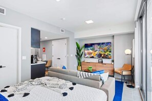 A modern hotel room with a large bed, a sofa, a desk, and a TV.