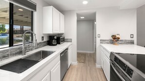 A modern kitchen with white cabinetry, a stainless steel sink, a built-in oven, and a coffee maker. - Luxurious Fairway Condo Resort (Palm Desert)