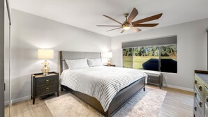 A bedroom with a bed, nightstands, a ceiling fan, a window with a view, and a dresser. - Luxurious Fairway Condo Resort (Palm Desert)
