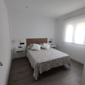Une chambre à coucher avec une tête de lit en bois, une couvre-lit à motifs, deux tables de chevet avec des lampes et une grande fenêtre avec des stores.