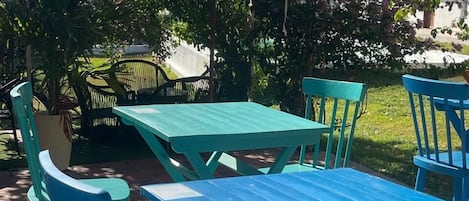 An outdoor patio with turquoise tables and chairs, surrounded by lush greenery and flowering plants.