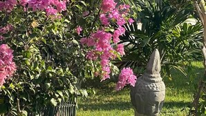 A stone Buddha statue in a garden with pink flowers and a stone bench. - Pousada Mali (Aracati)