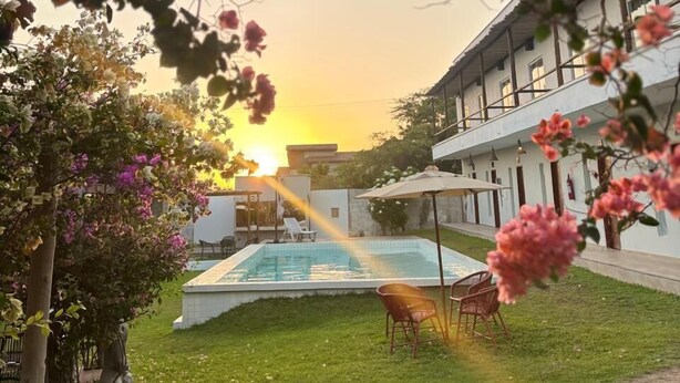 A pool area with a sunset view, surrounded by greenery and a building with multiple windows. - Pousada Mali (Aracati)
