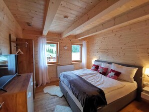 A wooden cabin bedroom with a bed, a TV, and two windows.