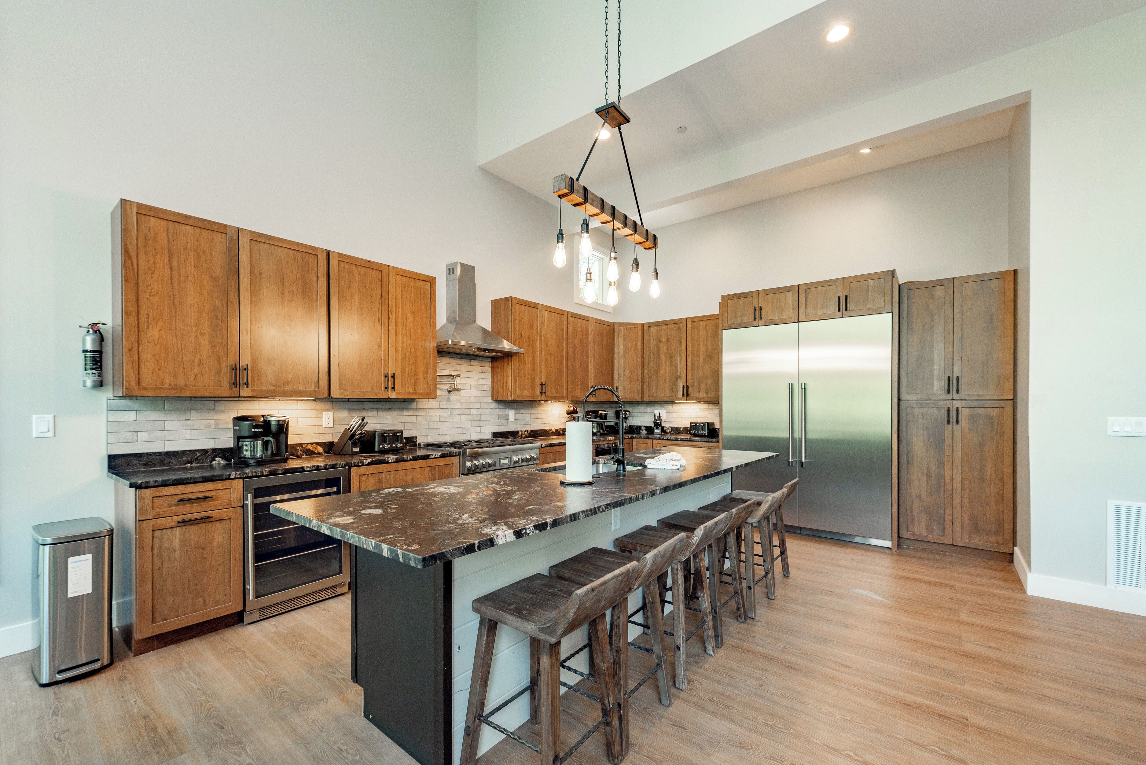 A modern kitchen with wooden cabinets, a stainless steel refrigerator, and a central island with bar stools.