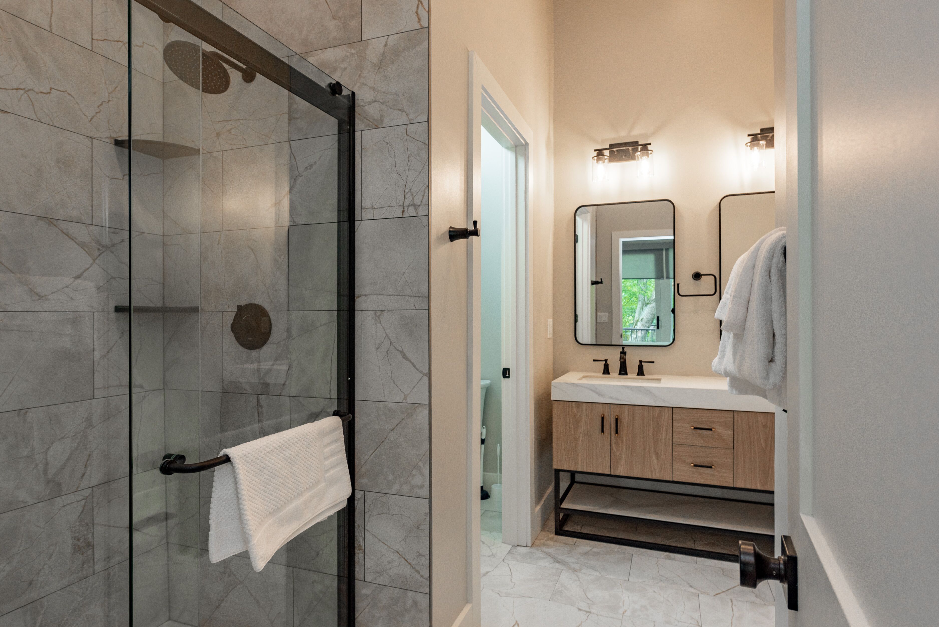 A modern bathroom with a glass-enclosed shower, a wooden vanity with a mirror, and a white towel hanging on a rack.