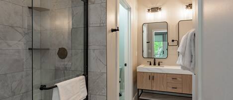 A modern bathroom with a glass-enclosed shower, a wooden vanity with a mirror, and a white towel hanging on a rack.