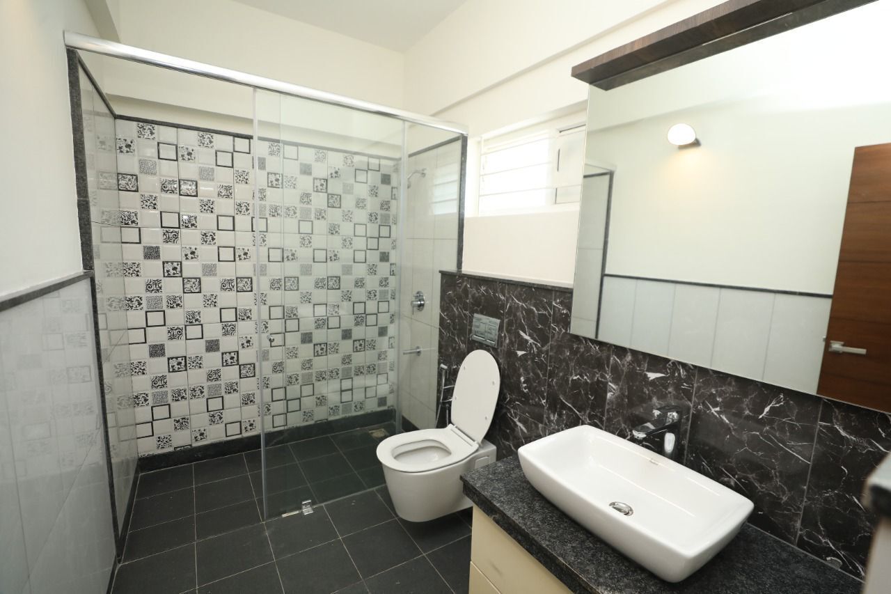 Un bany modern amb un box de dutxa de vidre, un vàter blanc i una superfície de marbre amb un lavabo.