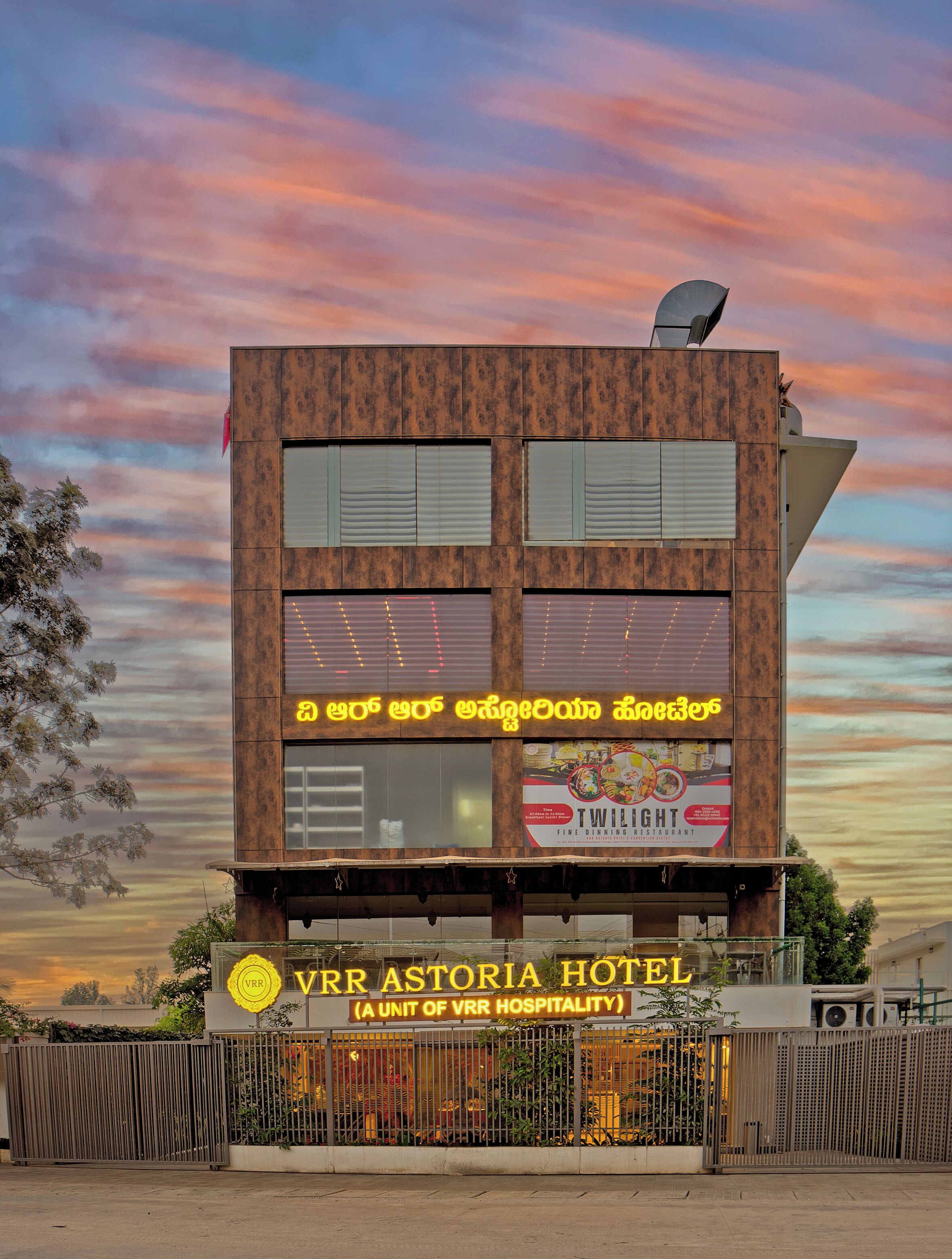 A hotel with a modern architectural design, featuring a prominent signboard with multilingual text and a visible restaurant advertisement.