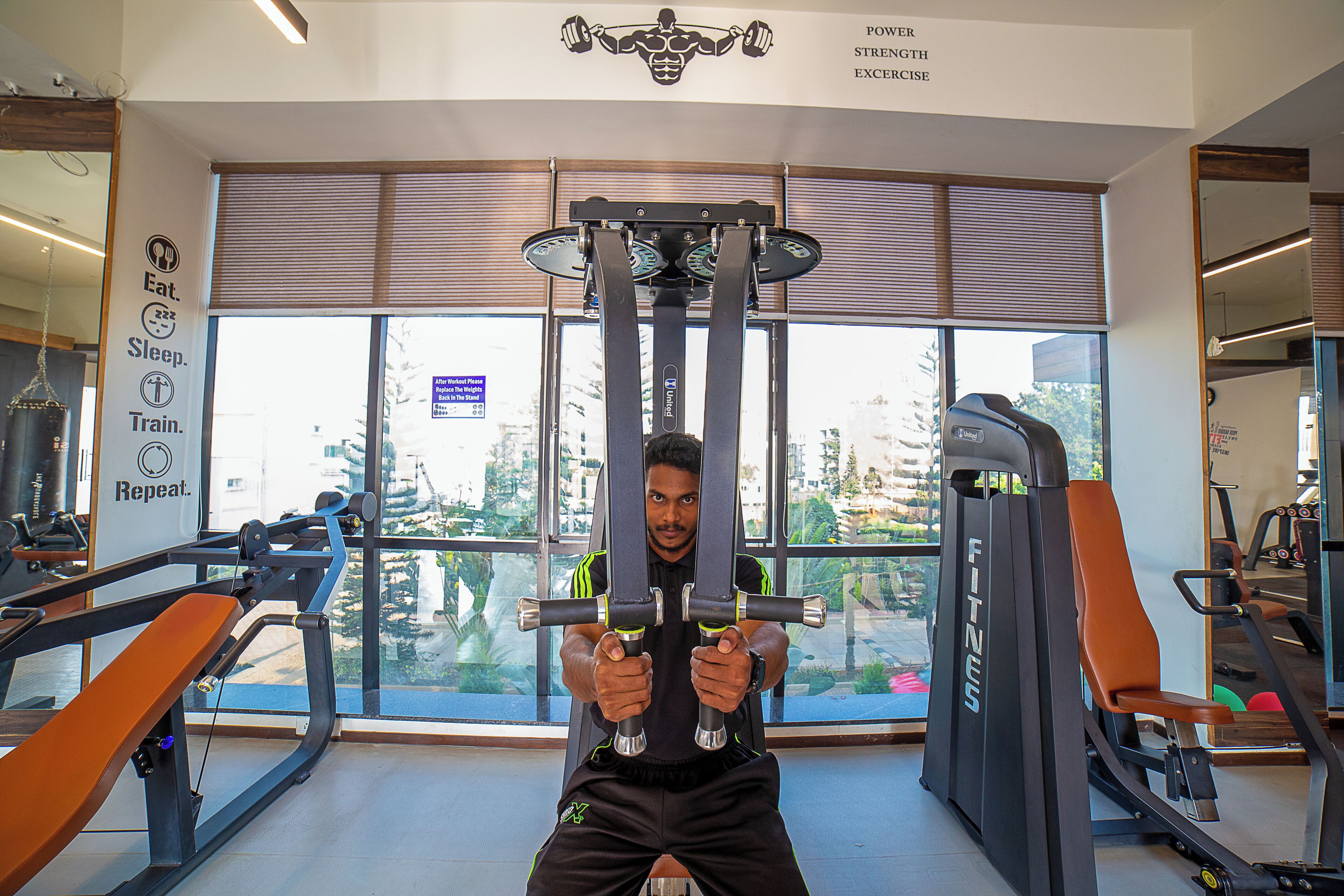 A gym with exercise equipment, large windows, and a motivational poster on the wall.