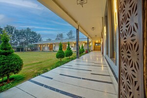 A covered walkway with a patterned railing, leading to a building with multiple doors and a well-maintained lawn with trimmed bushes.